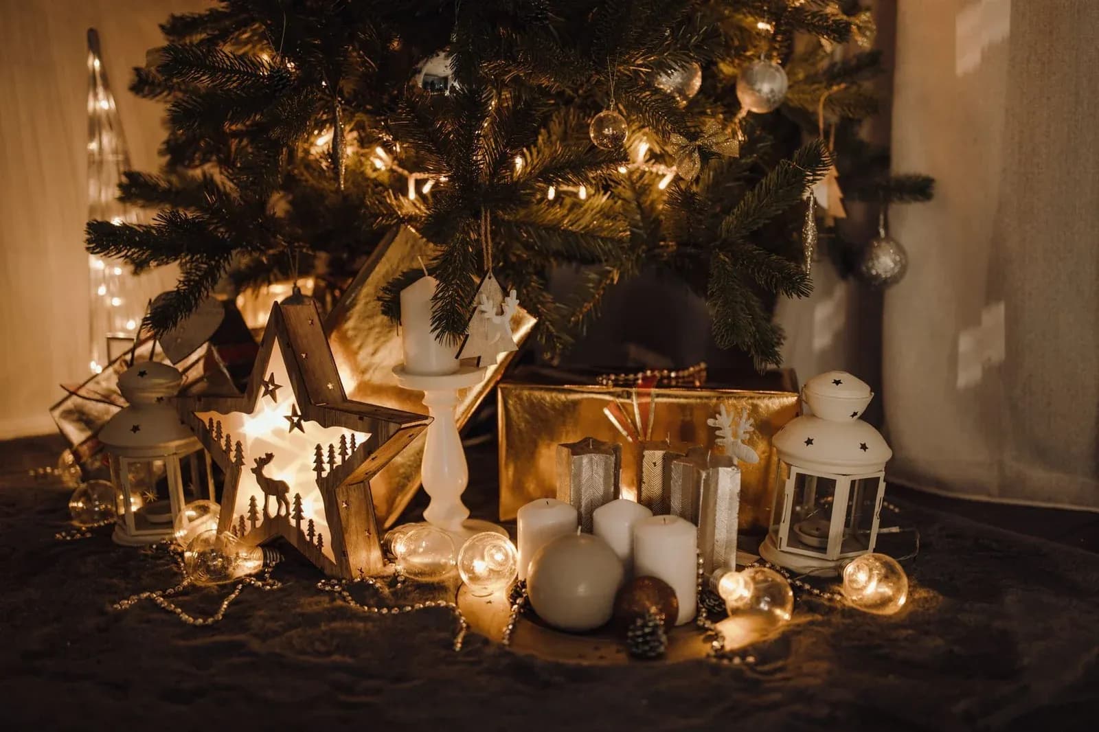 A softly lit Christmas tree with wrapped presents, candles and lanterns beneath it.