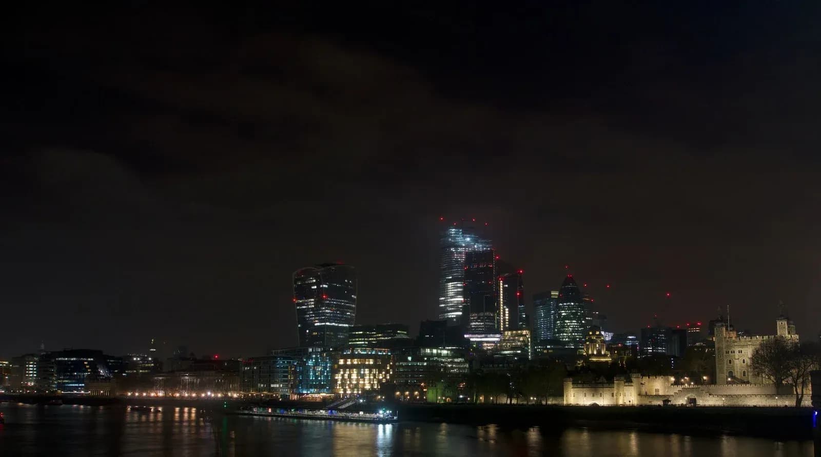 The City of London skyline lit up at night across the River Thames.