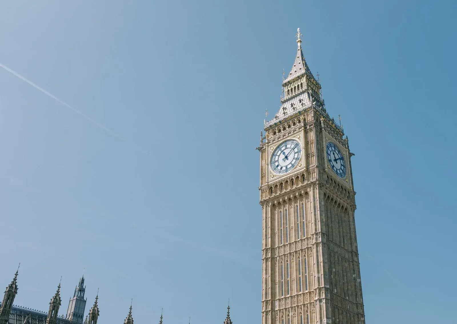 The Big Ben clock tower in Westminster against a bright blue sky in London.