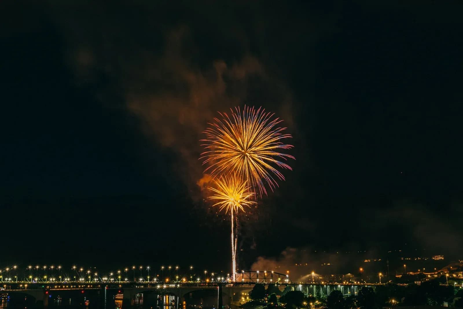 A golden firework bursting in the night sky above the lights of a city.