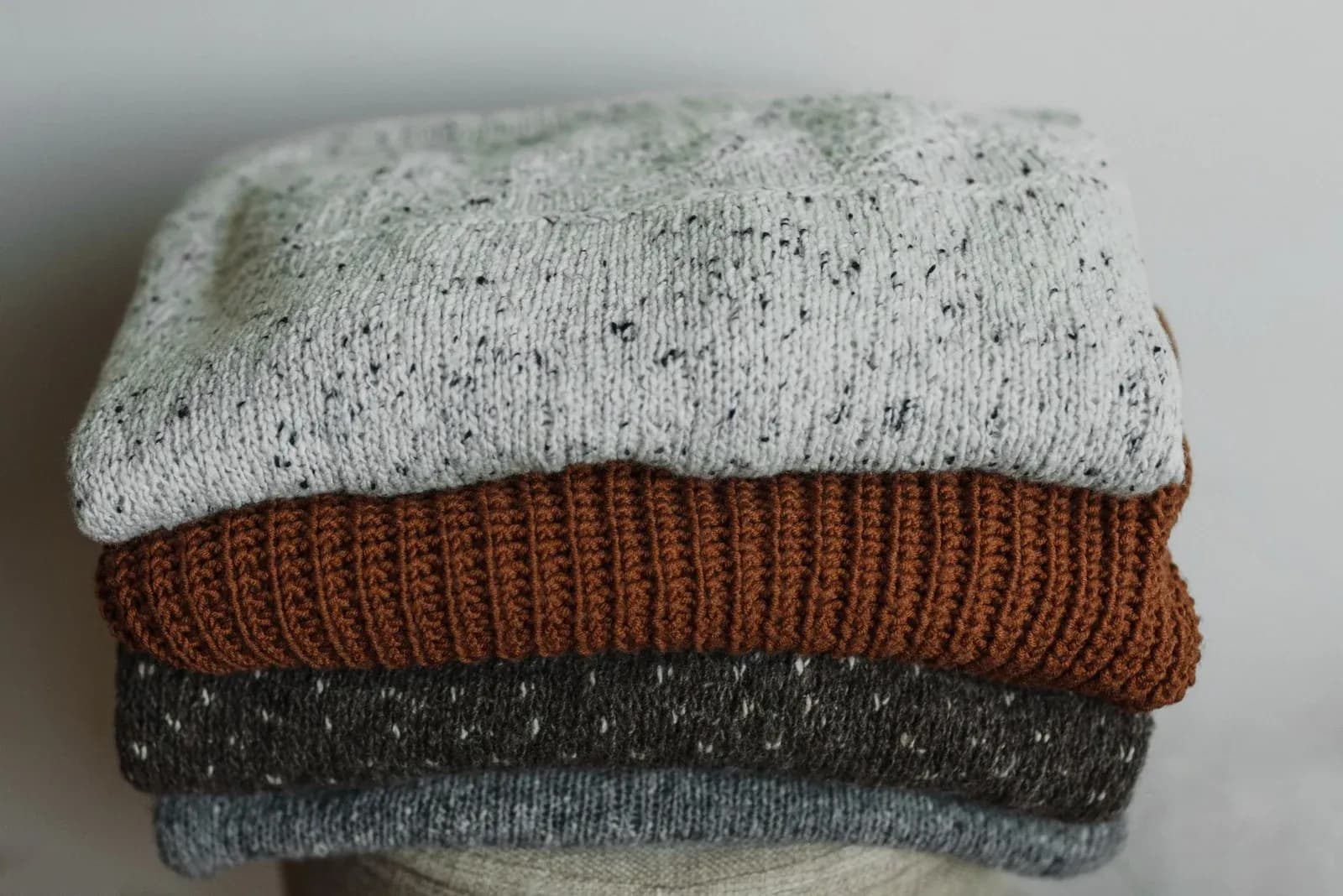 A neat stack of folded wool jumpers in grey, rust and charcoal.