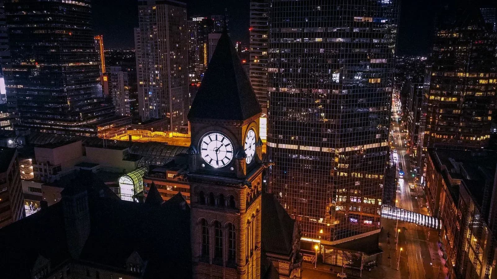 An illuminated clock tower stands among lit office towers in a city at night.