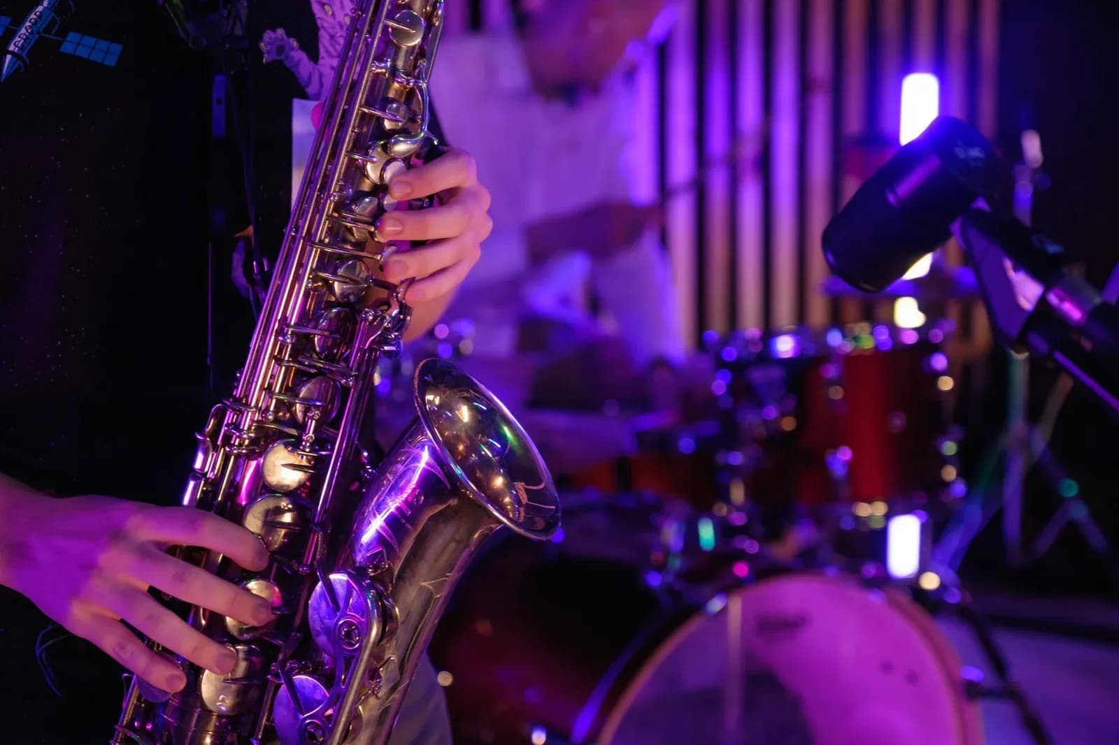 A saxophonist playing on a dimly lit jazz club stage beside a drum kit.