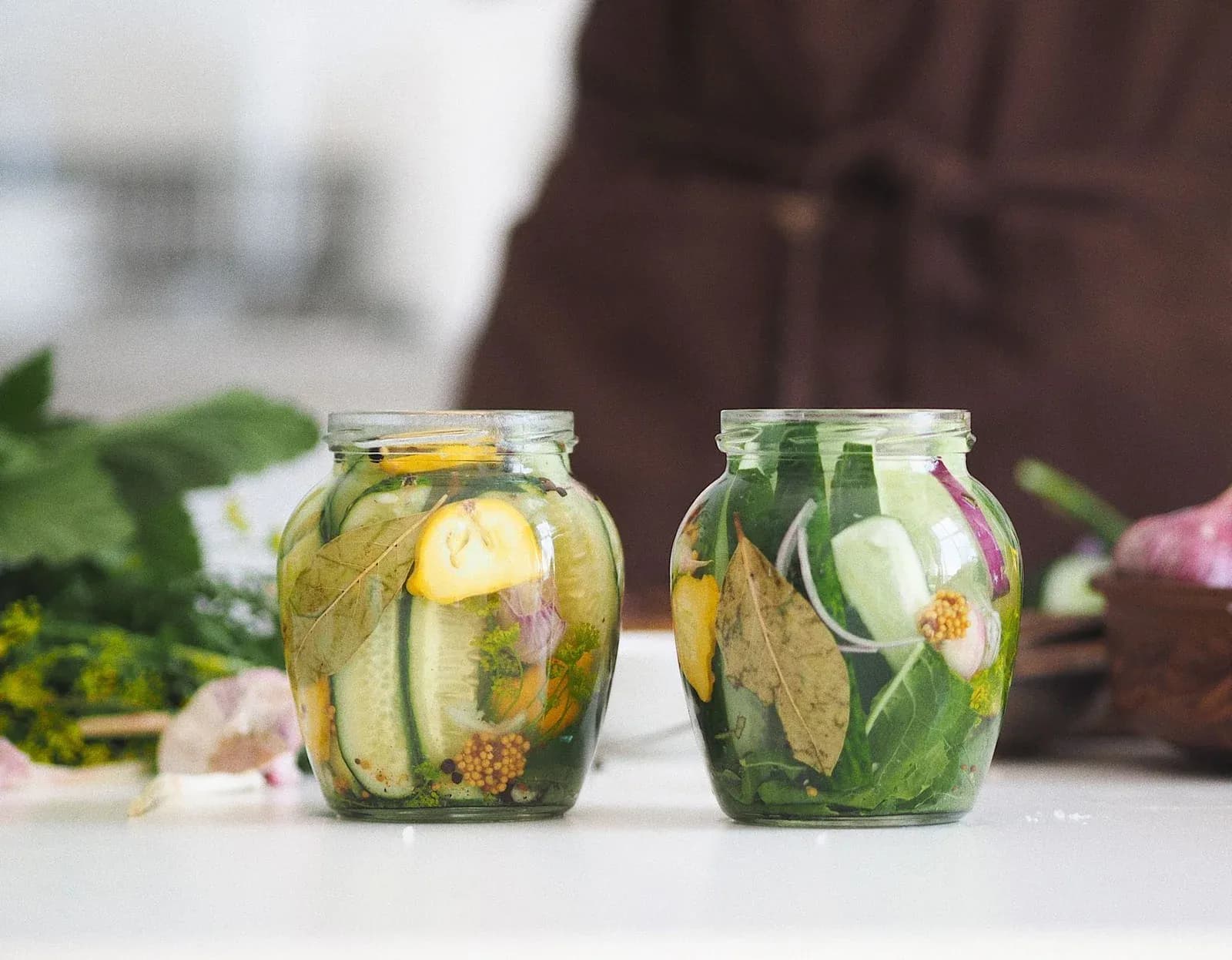Two glass jars of pickled cucumbers and cauliflower with dill on a kitchen table.