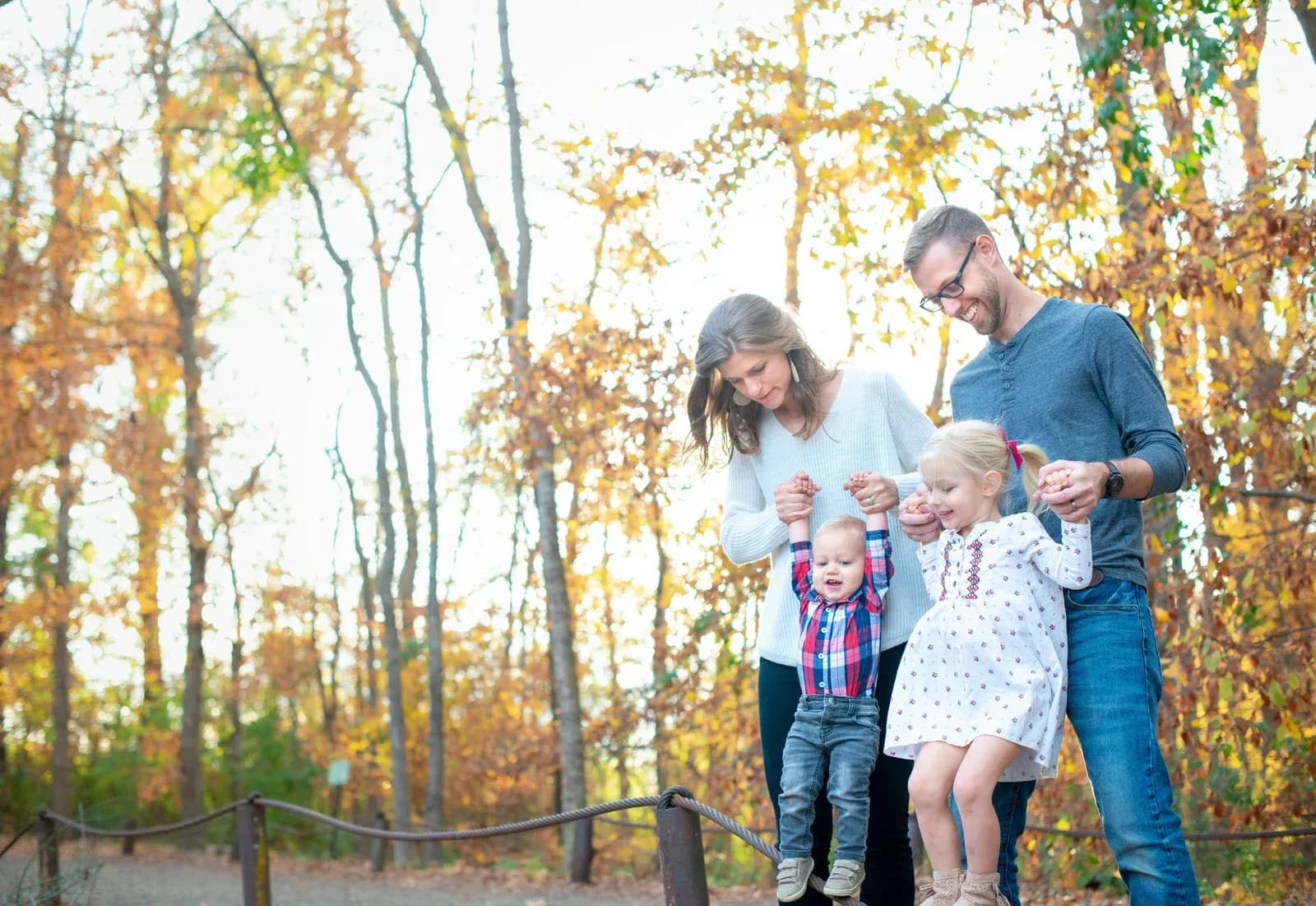 Two parents and their two children stand together among trees with golden autumn leaves.