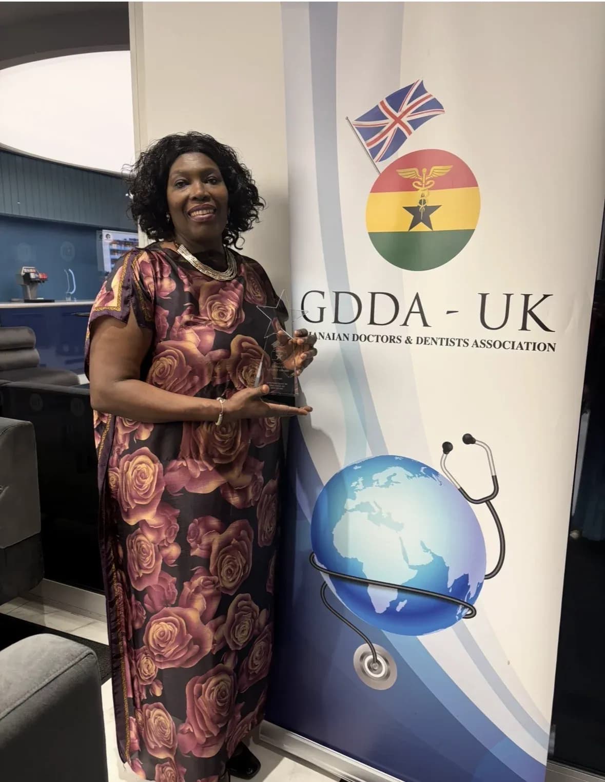 Dr I. Fortune Glavee holding an award beside a Ghanaian Doctors and Dentists Association UK banner