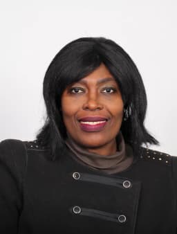 Dr I. Fortune Glavee in a black jacket against a light grey studio backdrop