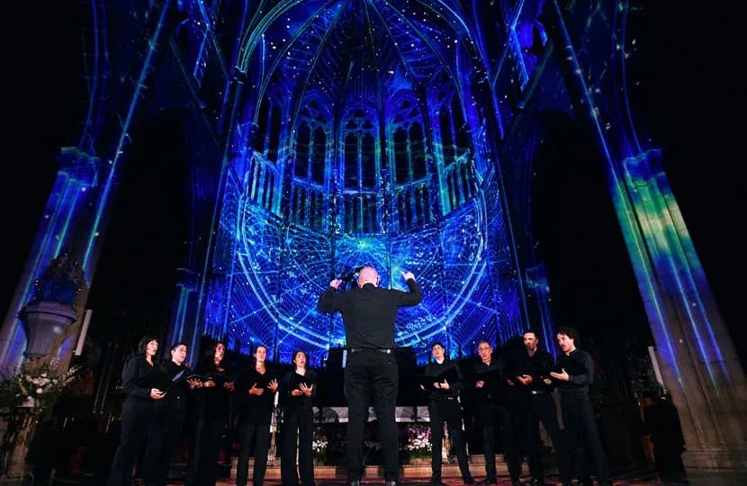 A cathedral apse lit in blue and green projection-mapped light during a LUMINISCENCE show, with a choir in silhouette