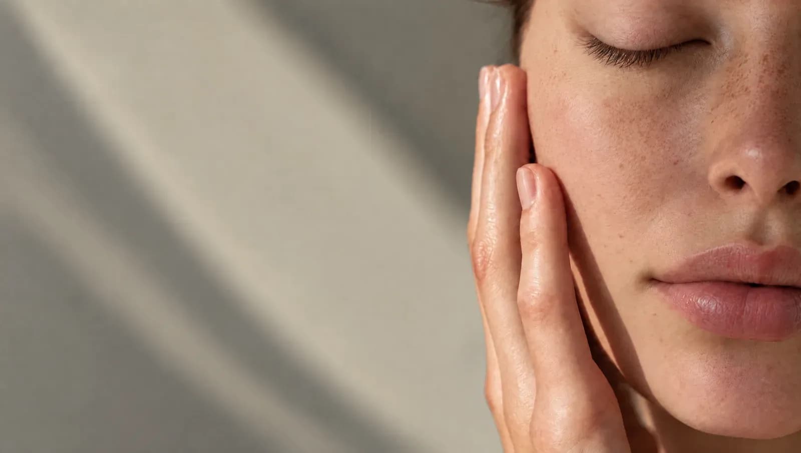 Close-up of a woman applying skincare to her cheek with her eyes closed