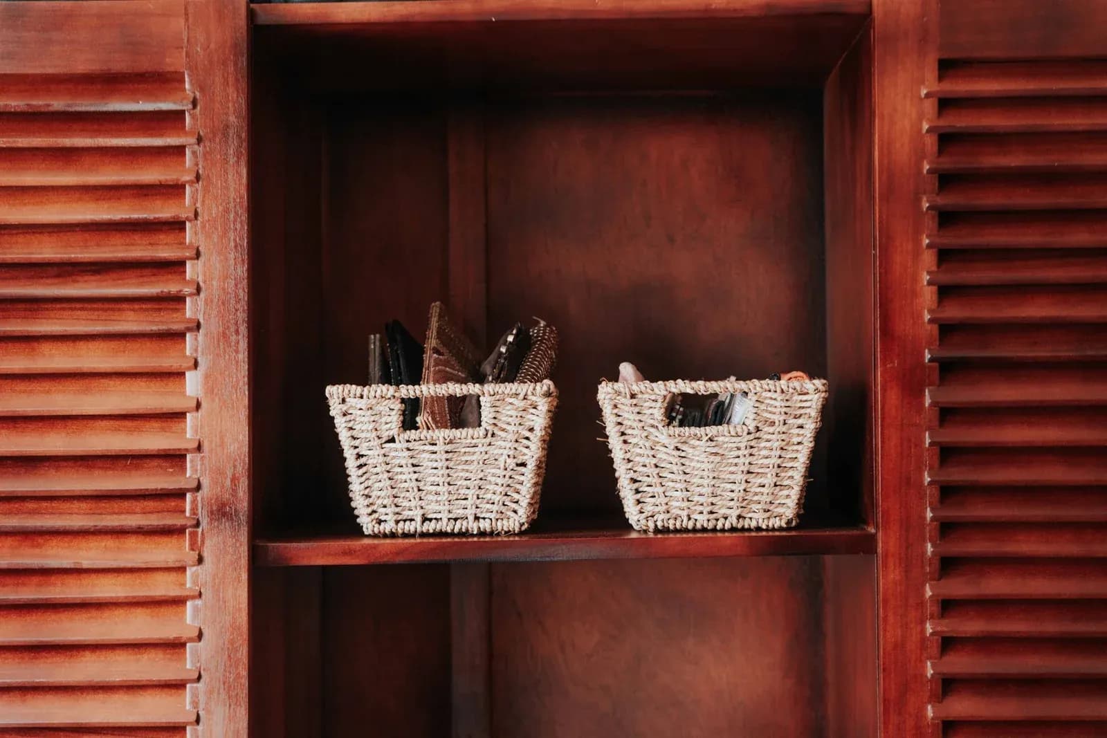 Two woven storage baskets on a wooden shelf between louvred cupboard doors.