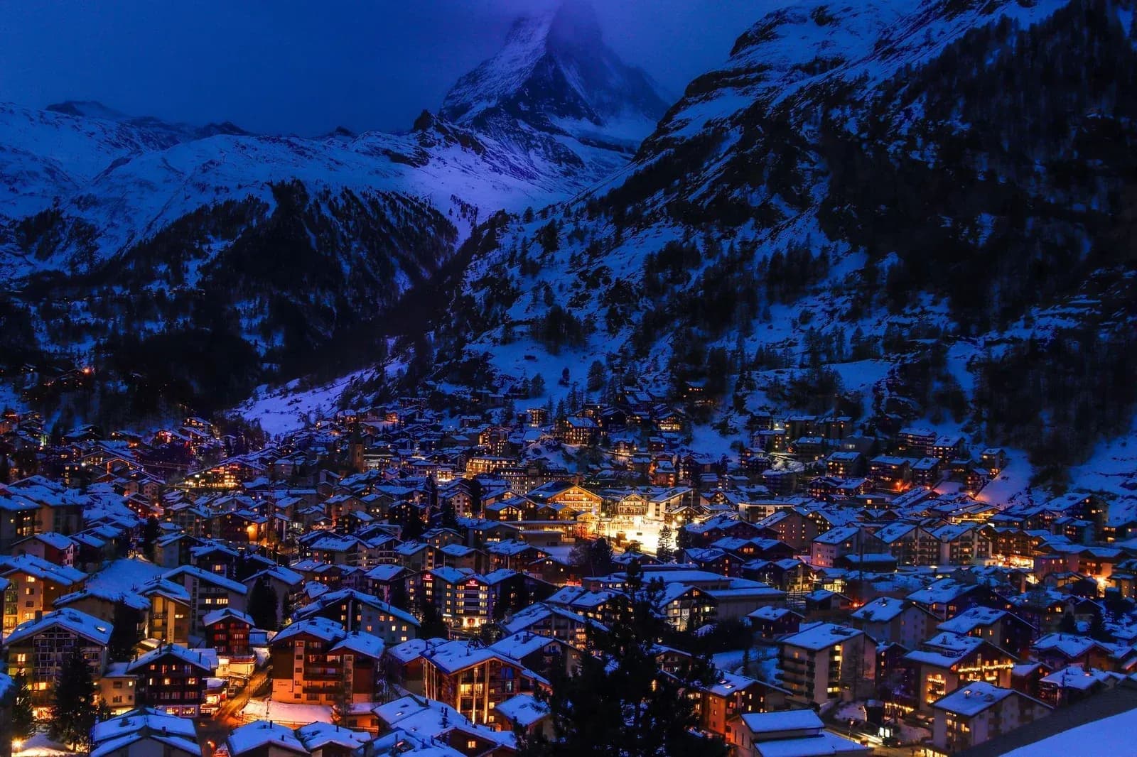 The snow-covered village of Zermatt lit up at blue hour beneath the Swiss Alps.