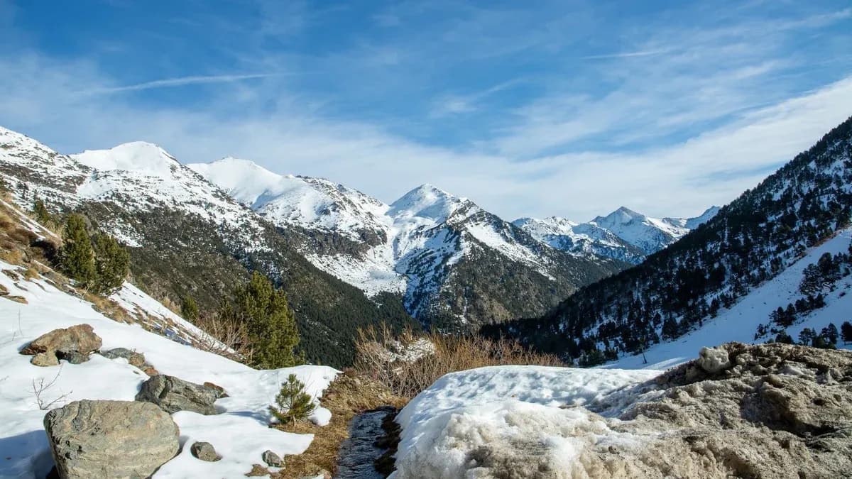 Snow-covered mountain peaks under a blue sky with rocks and snow in the foreground.