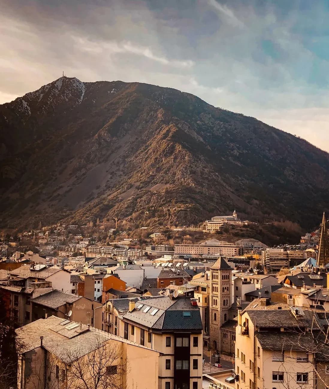 Rooftops of a mountain town in evening light below a large peak.