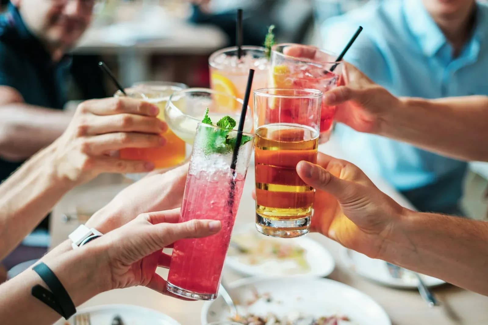 Friends raise and clink colourful drinks with straws over a lunch table.
