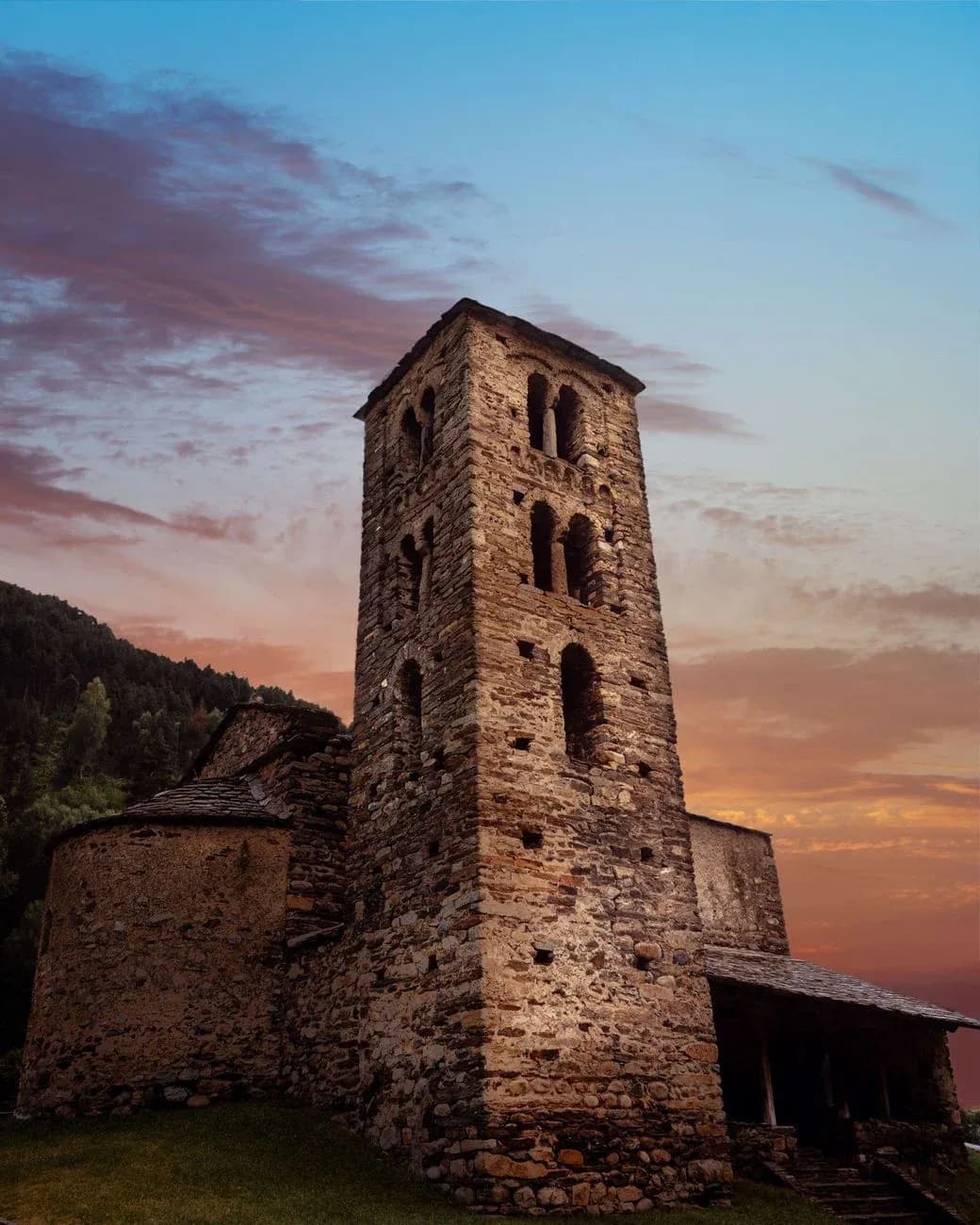 A Romanesque stone church with a square bell tower against an evening sky.