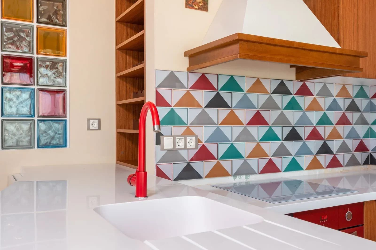 A bright kitchen with a white worktop, red tap and colourful geometric splashback tiles.