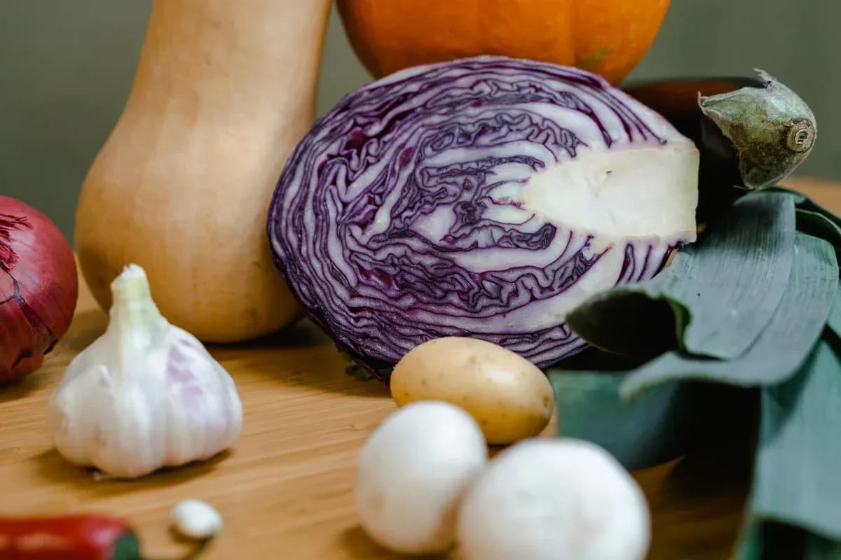 A halved red cabbage with squash, garlic, onion and sage leaves on a wooden board.