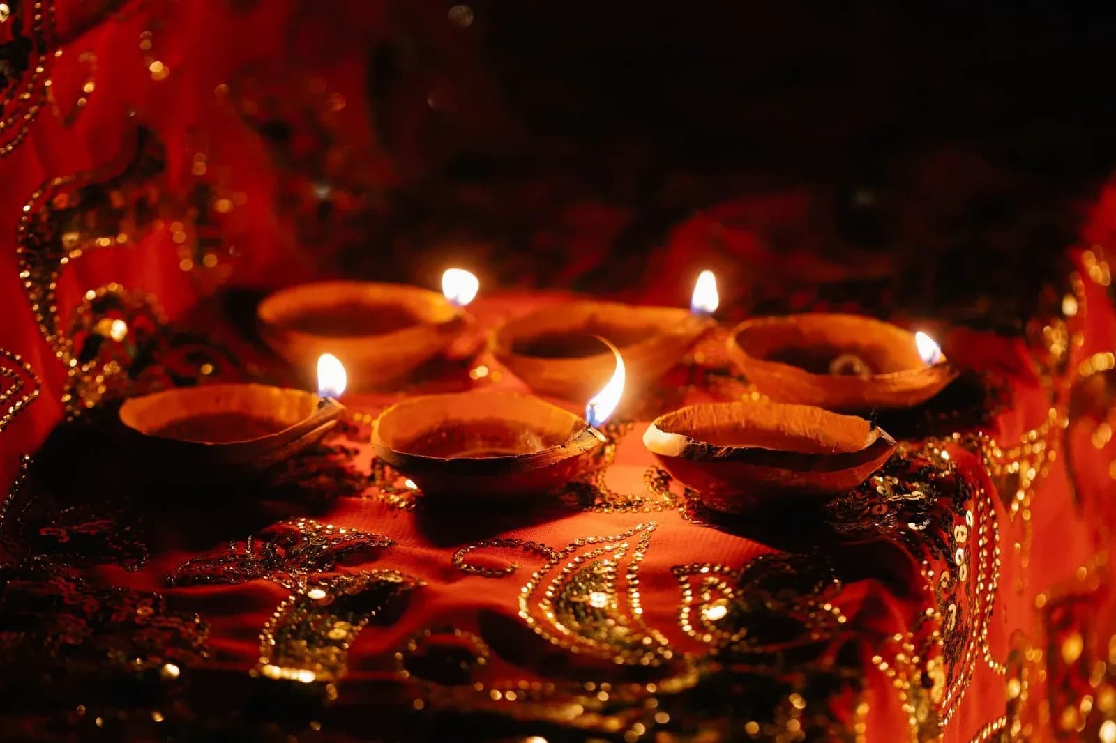 Lit clay oil lamps arranged on a red and gold cloth for Diwali.