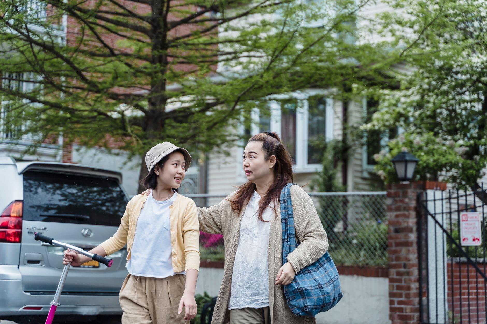 A mother and her teenage daughter walk outdoors together, smiling, the mother arm around her shoulder.