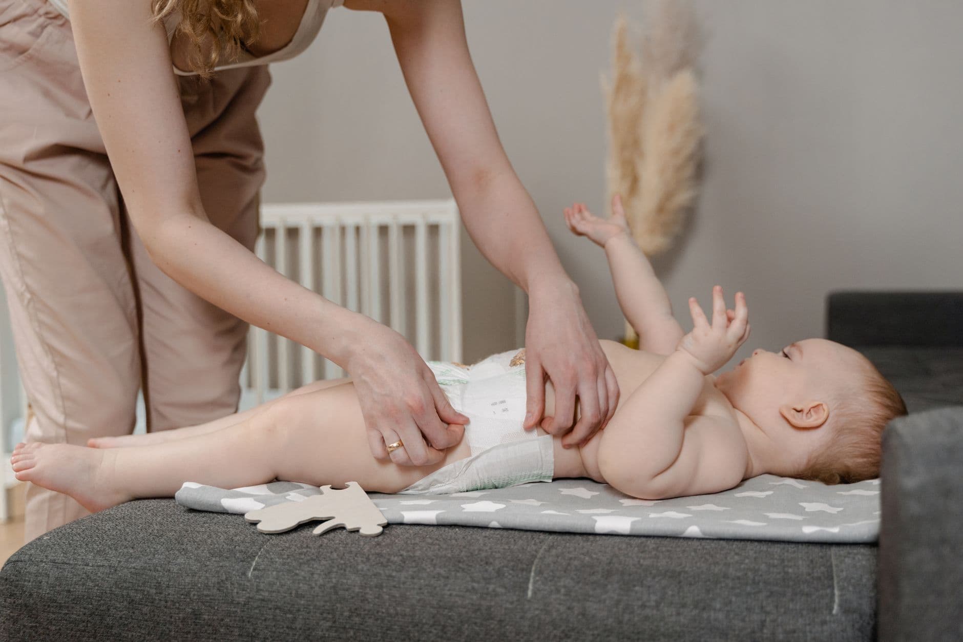 A mother gently changing her baby's diaper on a mat in a bright, calm home nursery