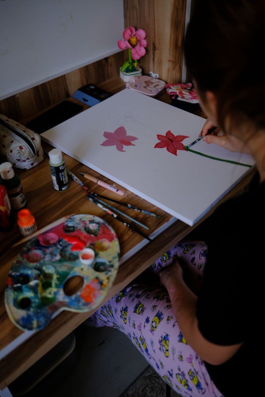 A young woman paints floral designs on canvas in a cozy, artistic studio setting.