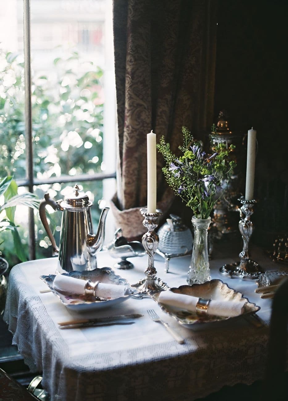 Beautifully arranged vintage table setting with candles and flower vase near a window in London.