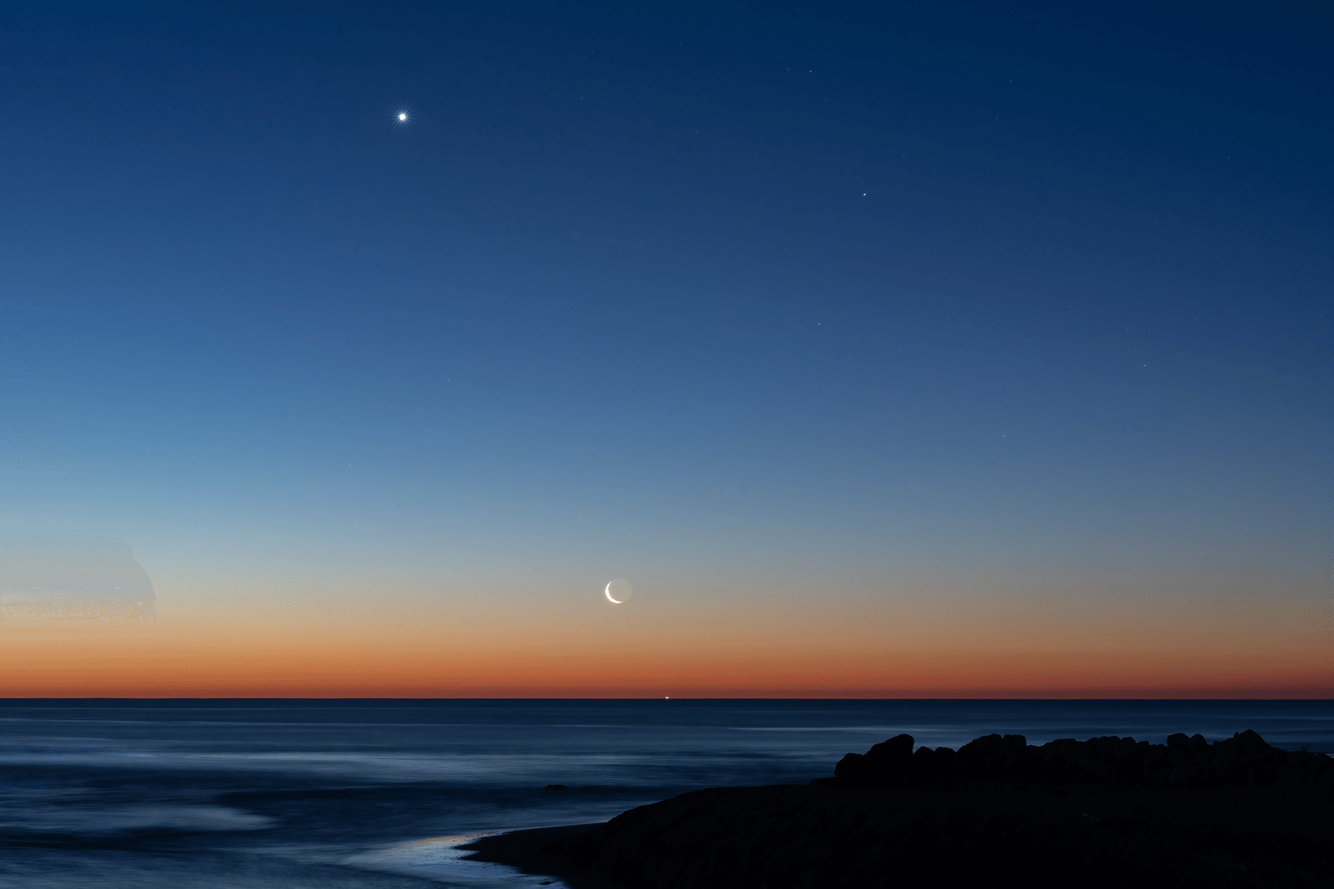 Captivating view of crescent moon and planets aligning over the ocean at twilight near Valencia, Spain.