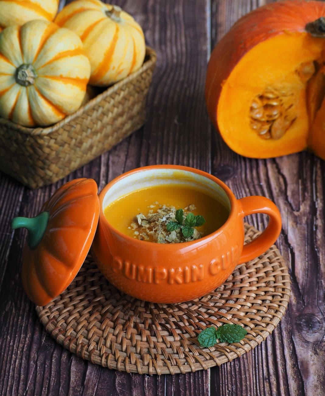 Close-up of fresh homemade pumpkin soup in an orange cup, surrounded by pumpkins.