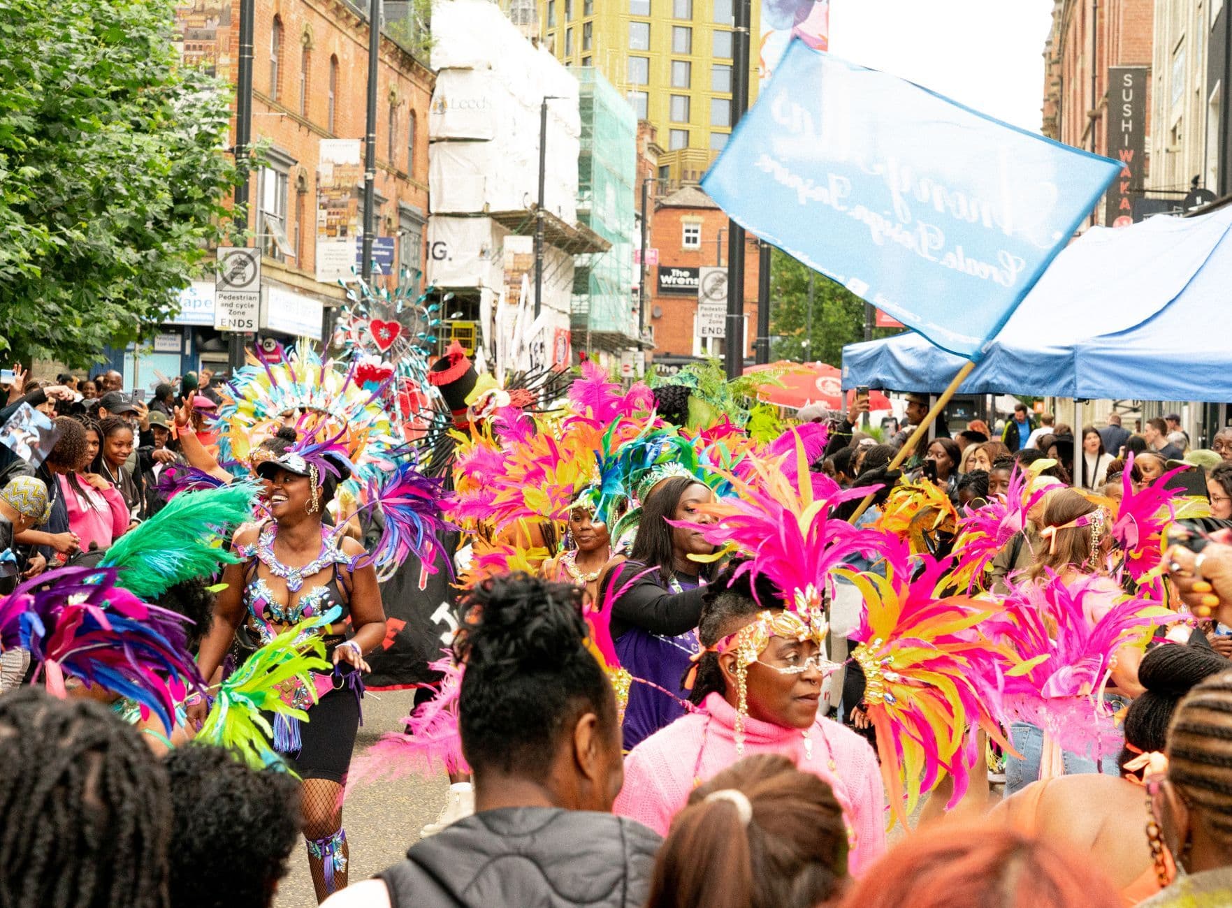 Colorful parade showcasing costumes and feathers in a lively urban street.