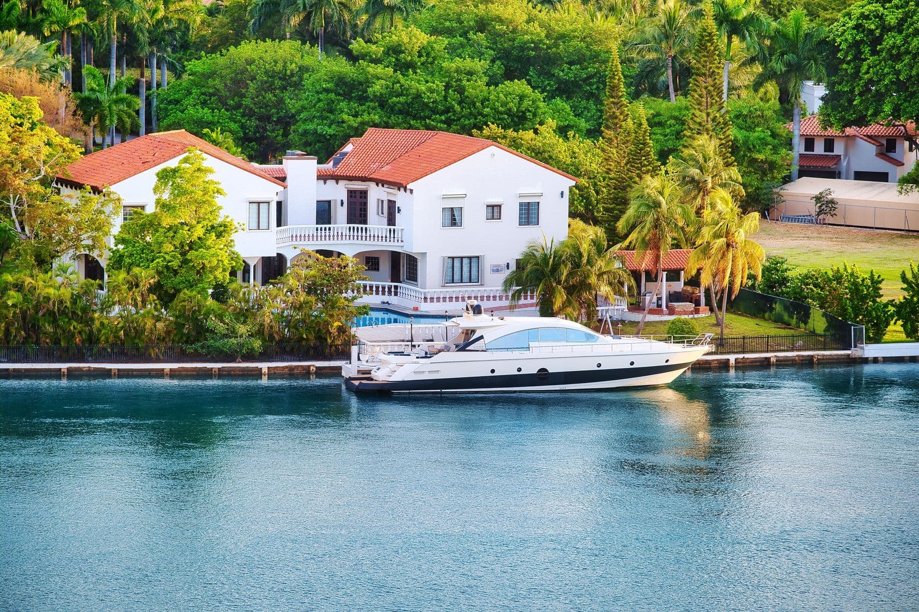 Elegant Miami luxury villa by the waterfront with a yacht docked nearby, unique architecture and tropical setting.