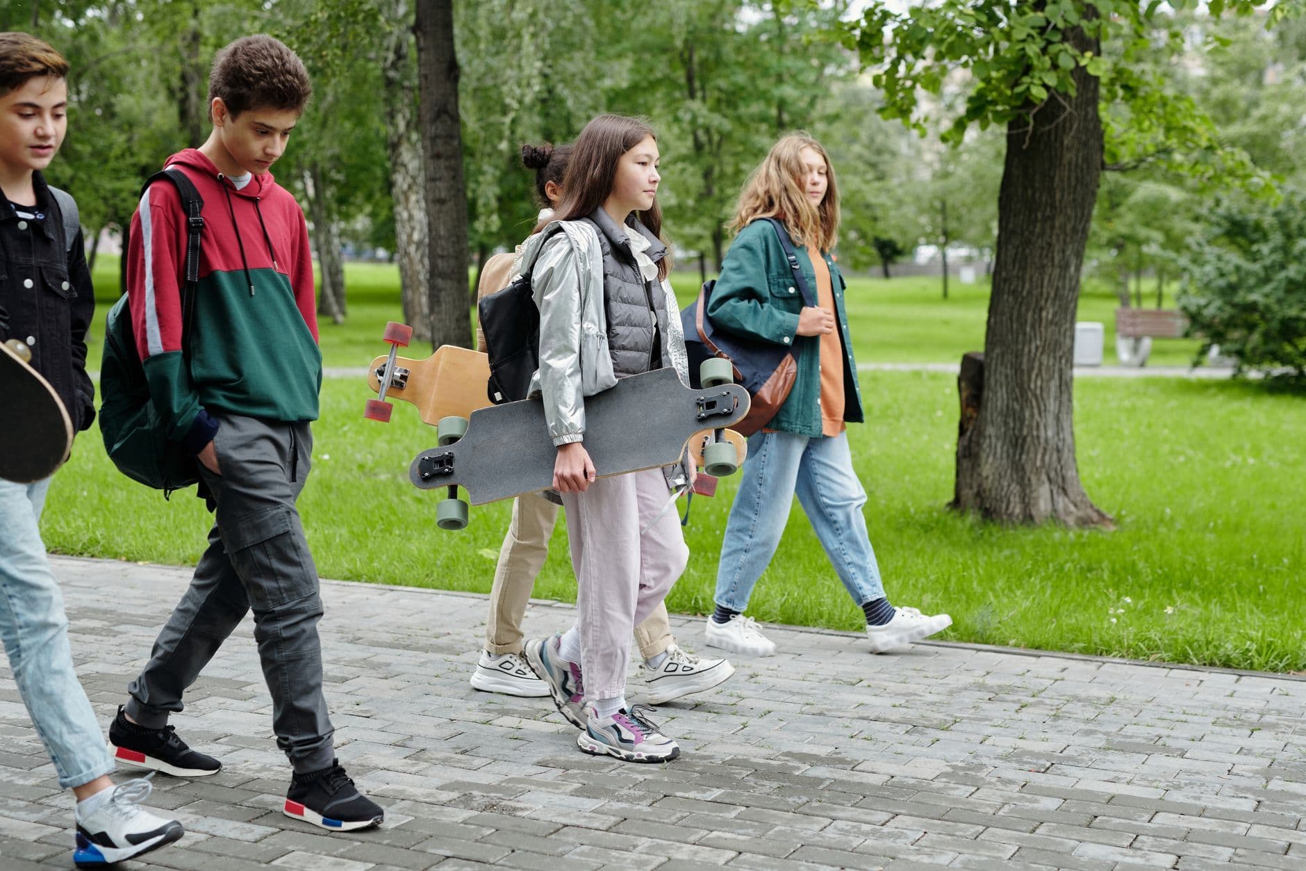 Group of teenagers strolling in a park carrying skateboards on a sunny day.