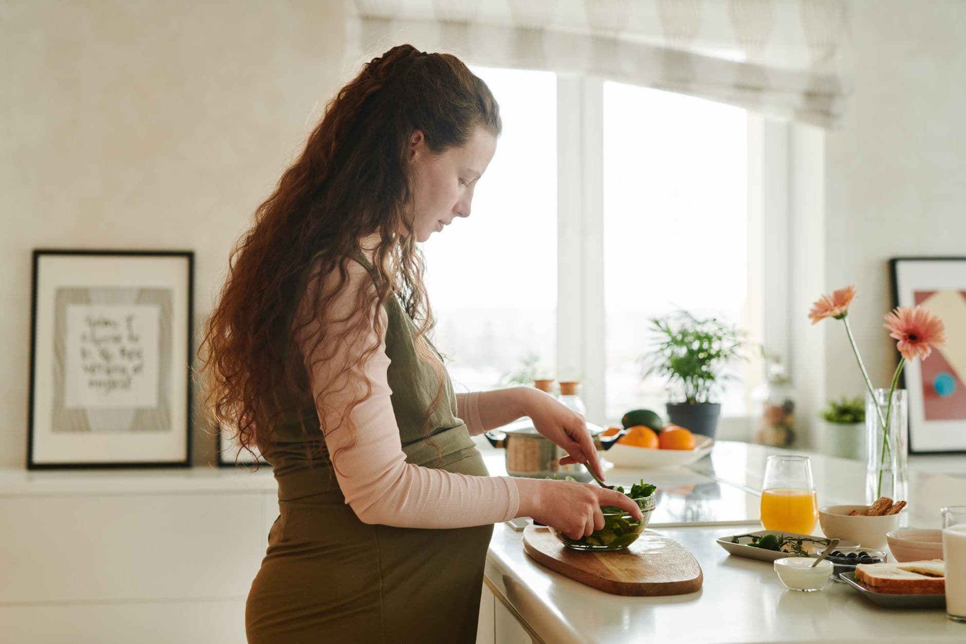Pregnant woman preparing a salad at a bright kitchen counter