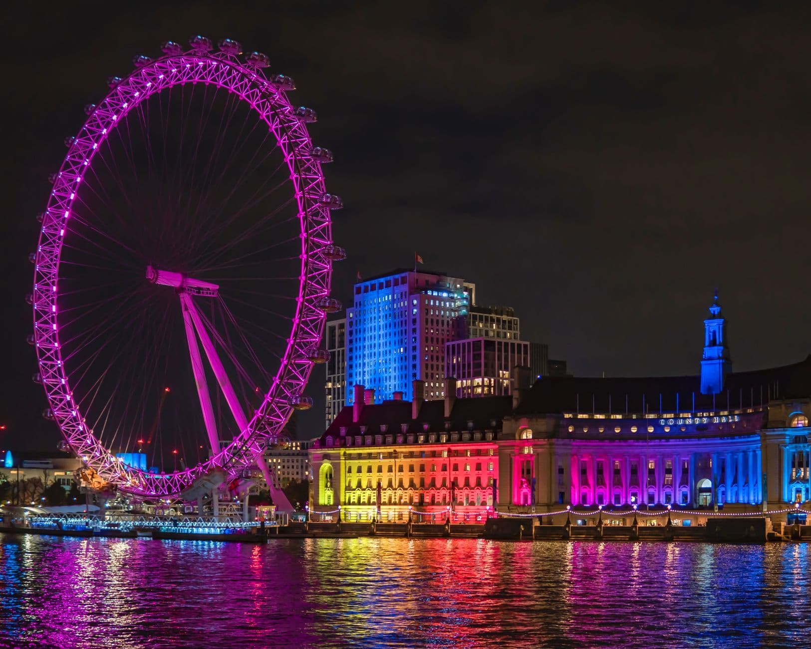 Stunning nighttime view of the illuminated London Eye reflecting on the River Thames.