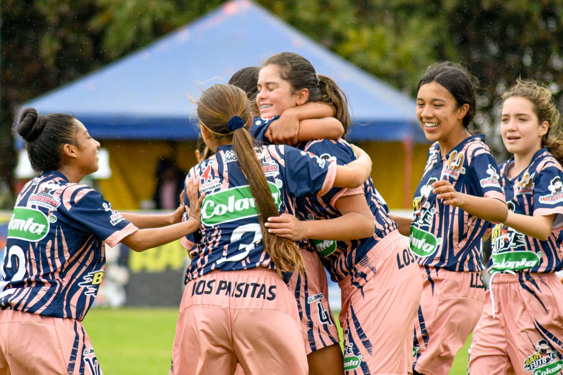 Young girls in soccer uniforms laughing and hugging on the field after a match