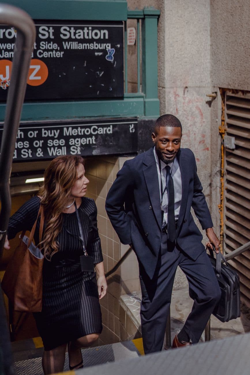 Two business professionals in formal attire exiting a New York City subway station.