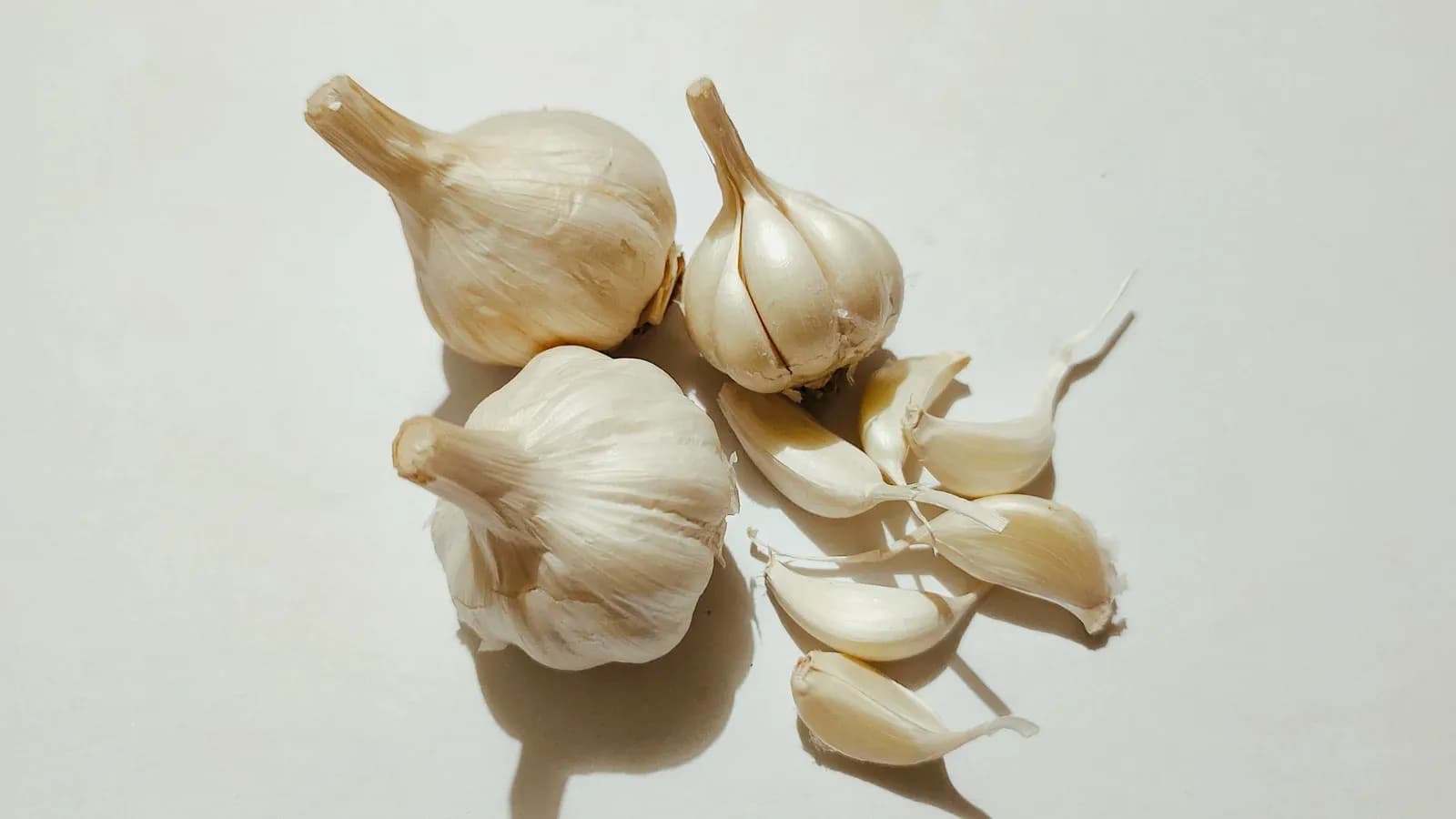 Whole garlic bulbs and loose cloves on a pale background.